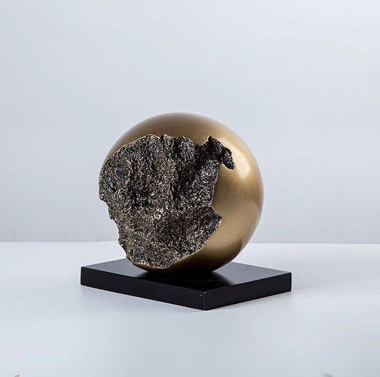 Rundt kugleornament i sort og guld på sokkel – moderne boligdekoration